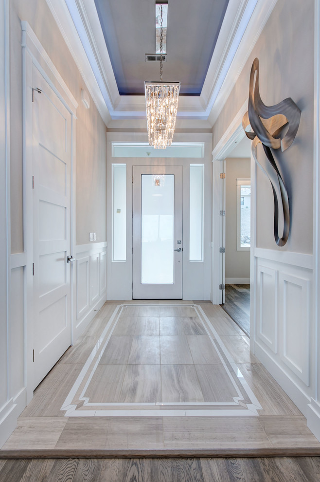 На фото: узкая прихожая среднего размера в стиле неоклассика (современная классика) с серыми стенами, полом из керамогранита, одностворчатой входной дверью, белой входной дверью и серым полом с