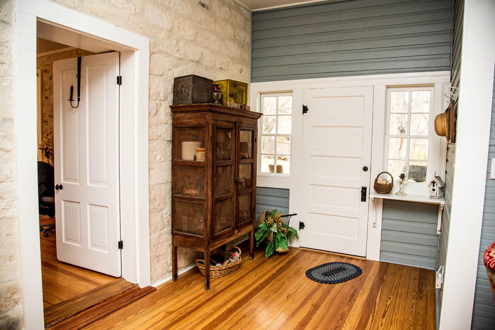 Bild på en mellanstor lantlig foajé, med grå väggar, mörkt trägolv, en enkeldörr, en vit dörr och brunt golv