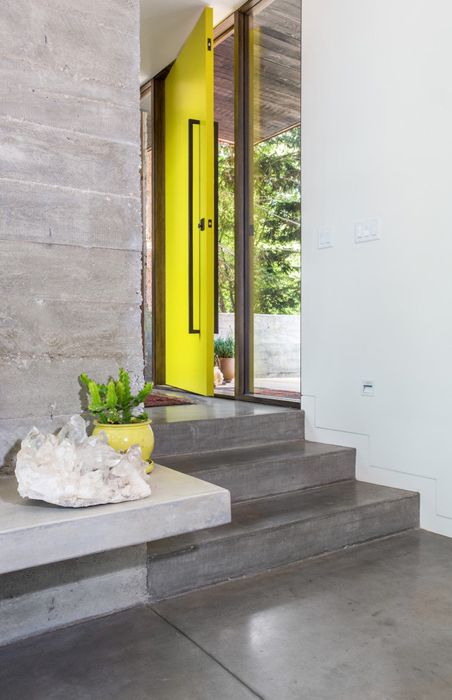 This is an example of an urban front door in Salt Lake City with concrete flooring, white walls, a single front door, a yellow front door and grey floors.