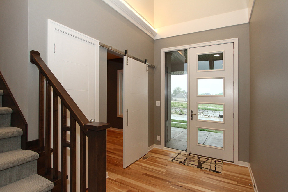 Exempel på en modern foajé, med grå väggar, ljust trägolv, en enkeldörr och en vit dörr