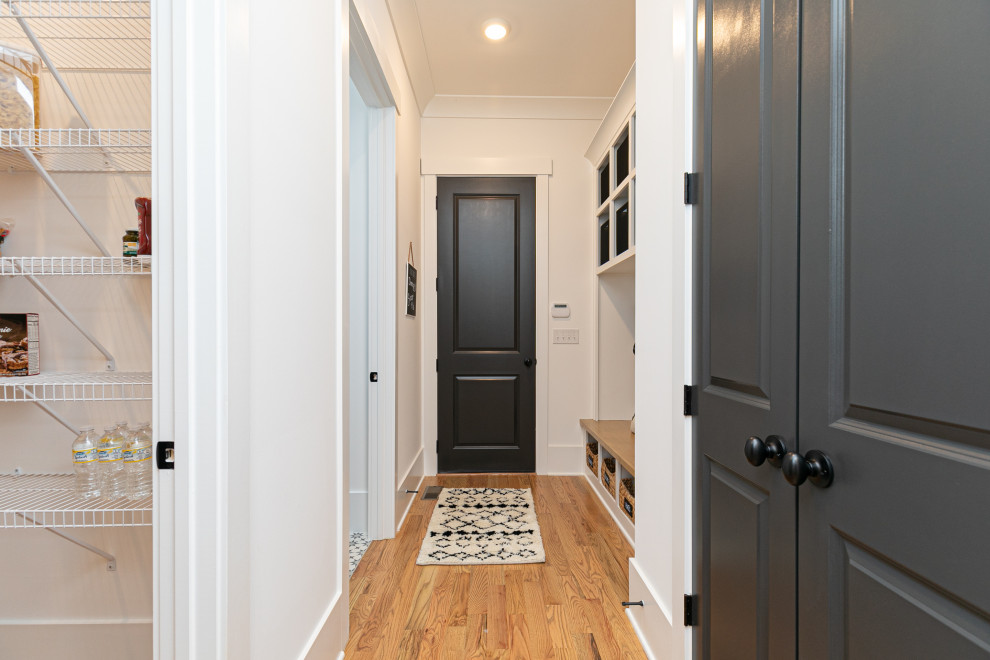Idéer för mellanstora amerikanska kapprum, med vita väggar, mellanmörkt trägolv, en enkeldörr, en svart dörr och brunt golv