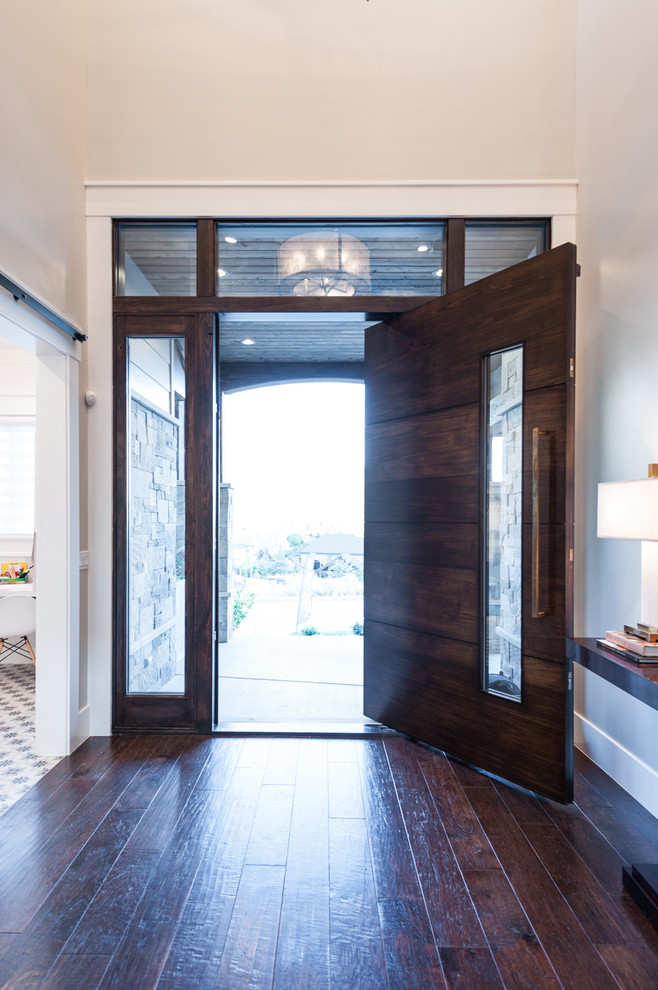 Modelo de puerta principal tradicional renovada de tamaño medio con paredes grises, suelo de madera oscura, puerta pivotante y puerta de madera oscura