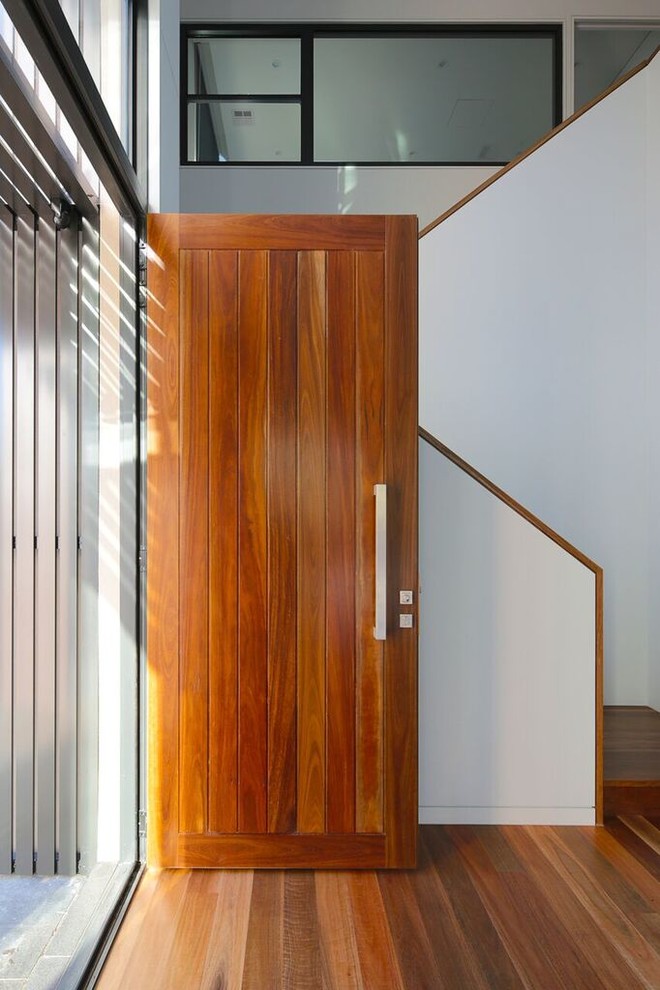 Cette photo montre une grande porte d'entrée tendance avec un mur blanc, un sol en bois brun, une porte simple, une porte en bois brun et un sol marron.