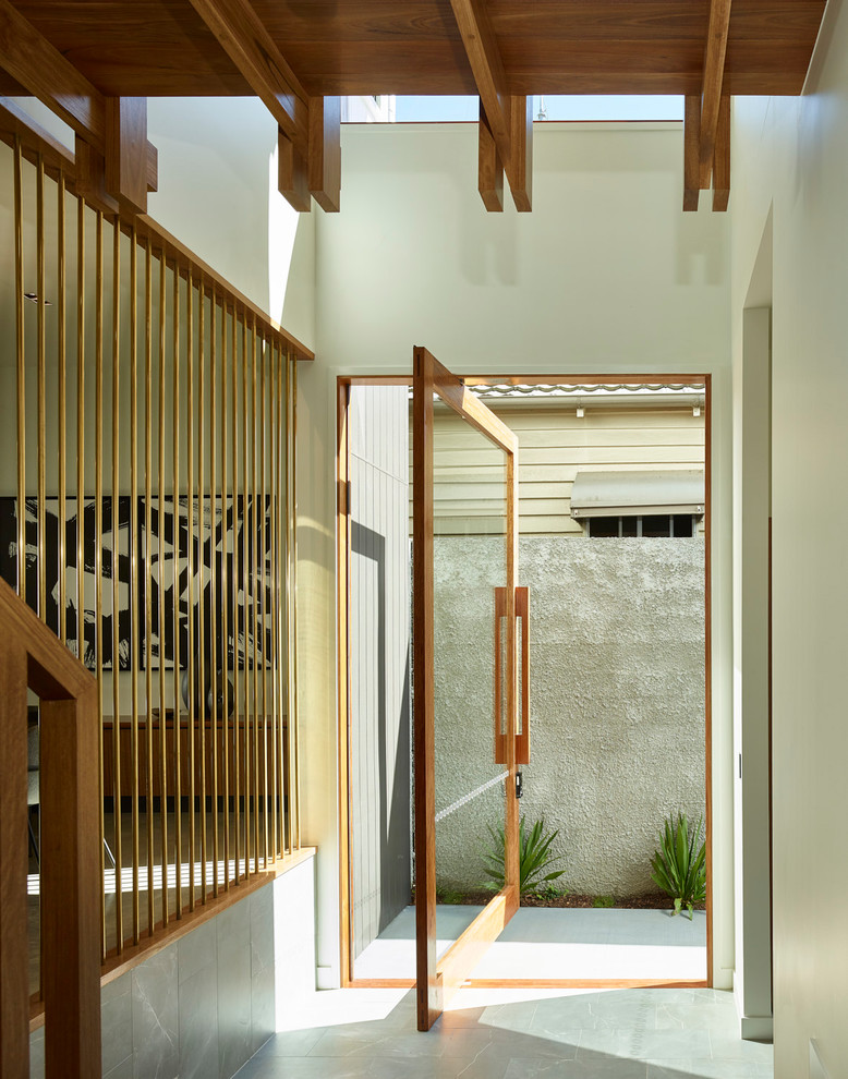 Modelo de puerta principal actual de tamaño medio con paredes blancas, suelo de travertino, puerta pivotante, puerta de madera en tonos medios y suelo gris