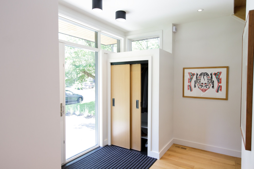 Diseño de distribuidor minimalista de tamaño medio con paredes blancas, suelo de madera en tonos medios, puerta doble y puerta blanca