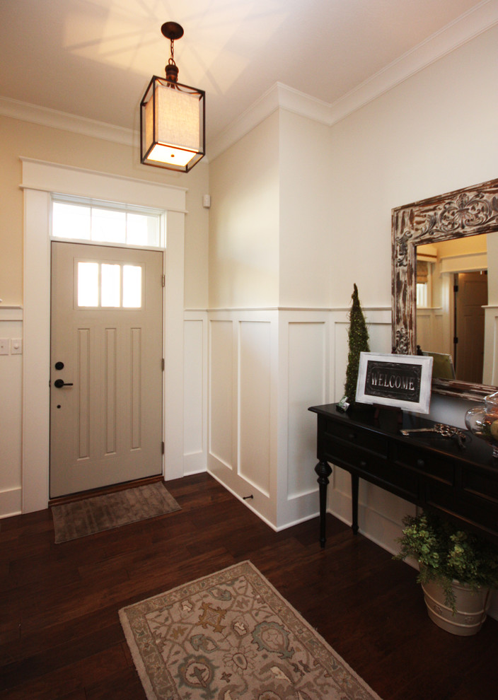 Cette photo montre un hall d'entrée chic avec un mur beige, un sol en bois brun, une porte simple et une porte grise.