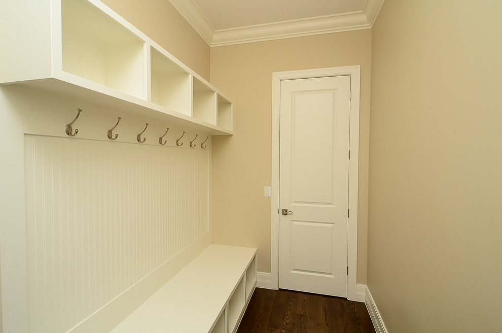Cette photo montre une grande entrée chic avec un vestiaire, un mur beige et un sol en bois brun.
