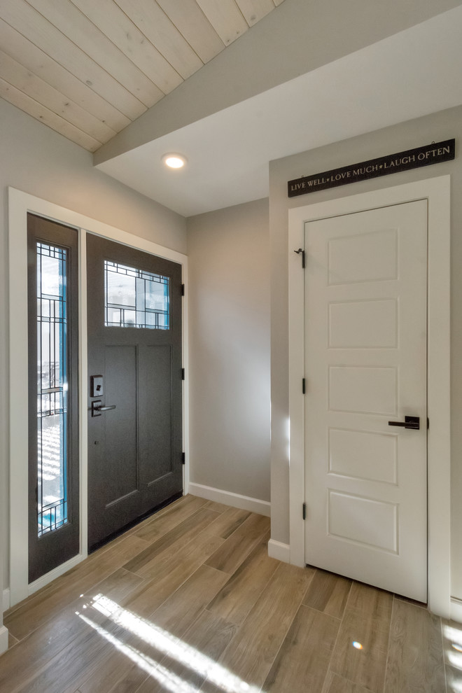 На фото: входная дверь среднего размера в стиле неоклассика (современная классика) с серыми стенами, полом из керамогранита, одностворчатой входной дверью, черной входной дверью и коричневым полом с