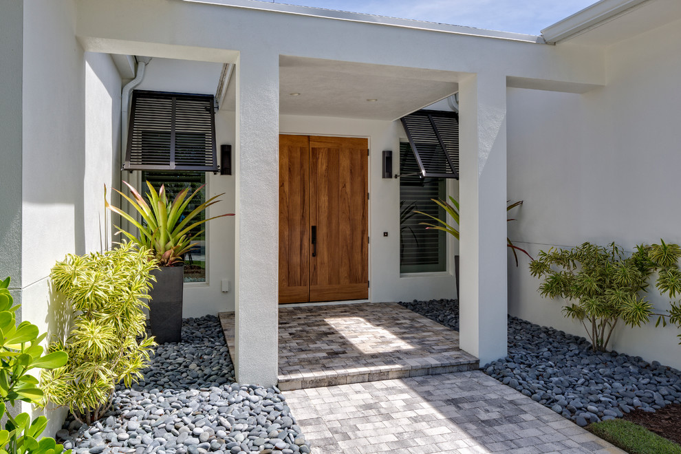 Modelo de puerta principal exótica grande con paredes blancas, suelo de cemento, puerta doble y puerta de madera en tonos medios