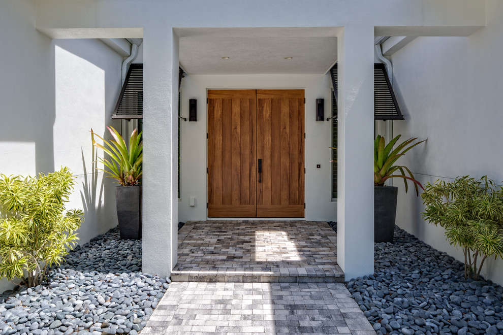 マイアミにある広いトロピカルスタイルのおしゃれな玄関ドア (白い壁、コンクリートの床、木目調のドア) の写真