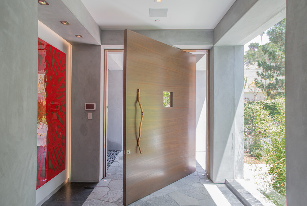 Idee per un corridoio contemporaneo con pareti grigie, pavimento in pietra calcarea, una porta a pivot, una porta in legno chiaro e pavimento grigio