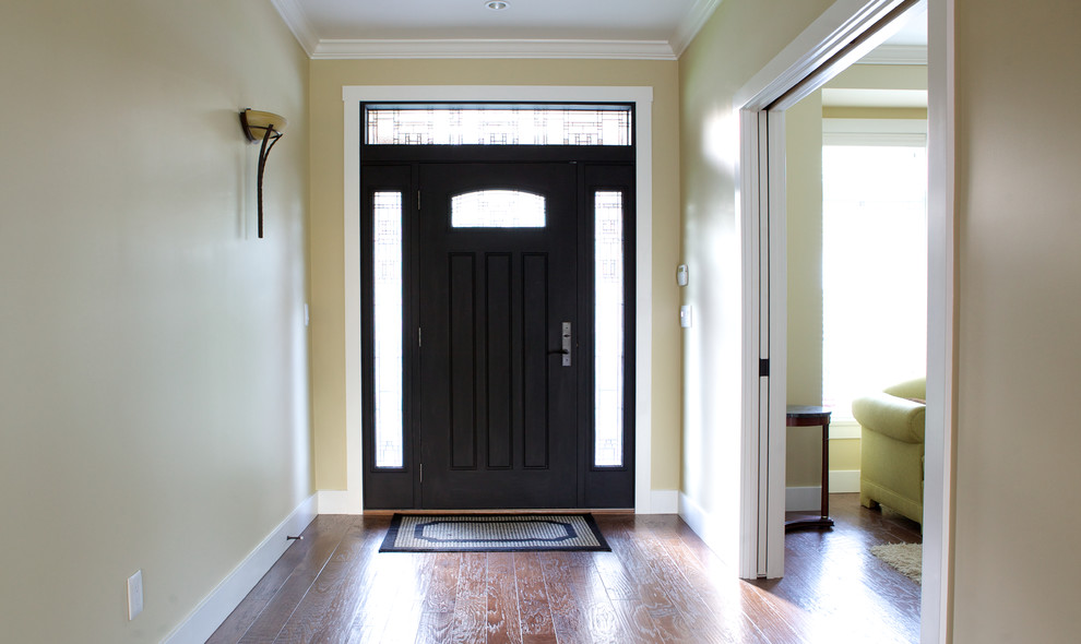 Foto di un corridoio classico con pareti gialle, pavimento in legno massello medio, una porta a pivot e una porta nera