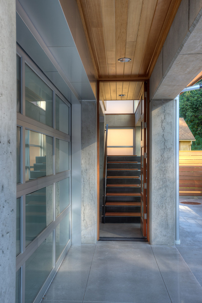 Modelo de puerta principal moderna pequeña con paredes beige, suelo de cemento, puerta simple, puerta de madera clara y suelo beige