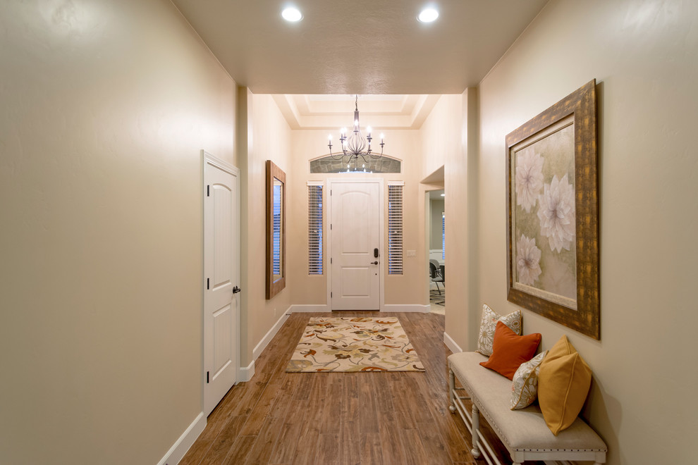 Ispirazione per un corridoio chic di medie dimensioni con pareti beige, pavimento in legno massello medio, una porta singola e una porta bianca