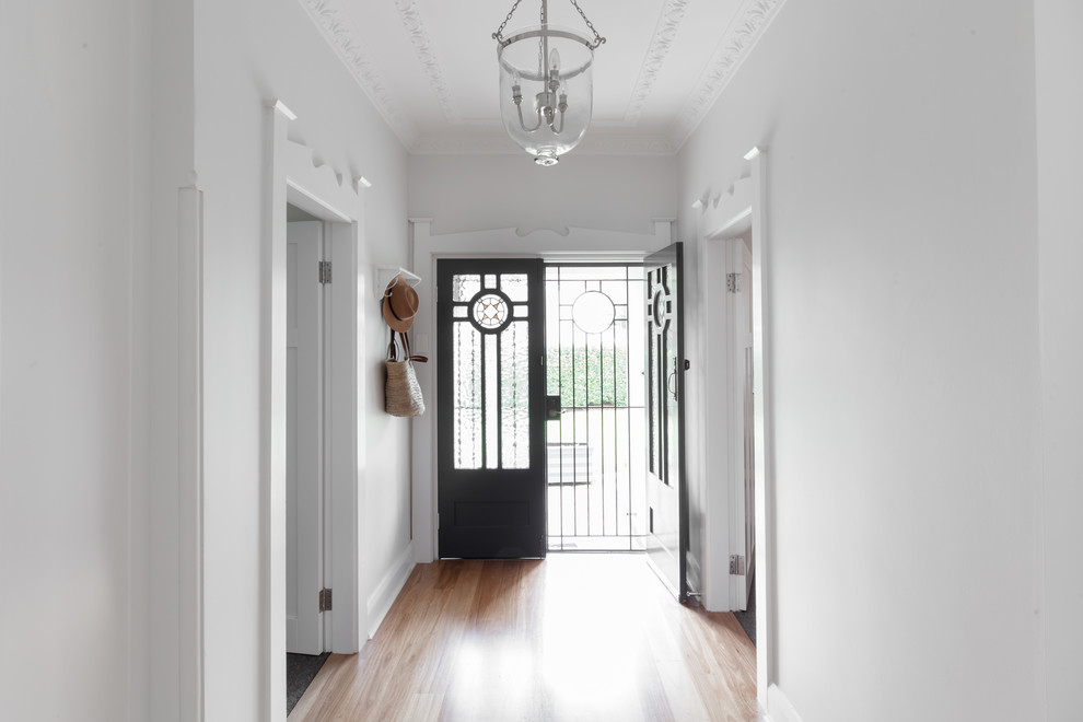 Réalisation d'une entrée tradition de taille moyenne avec un couloir, un mur blanc, un sol en bois brun, une porte double, une porte noire et un sol marron.