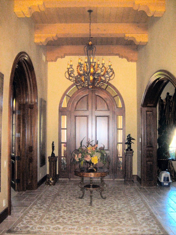 Aménagement d'un grand hall d'entrée méditerranéen avec un mur jaune, un sol en travertin, une porte double et une porte en bois foncé.