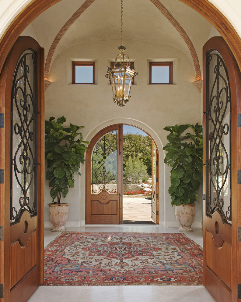 На фото: фойе в средиземноморском стиле с бежевыми стенами, мраморным полом, двустворчатой входной дверью, входной дверью из дерева среднего тона и белым полом
