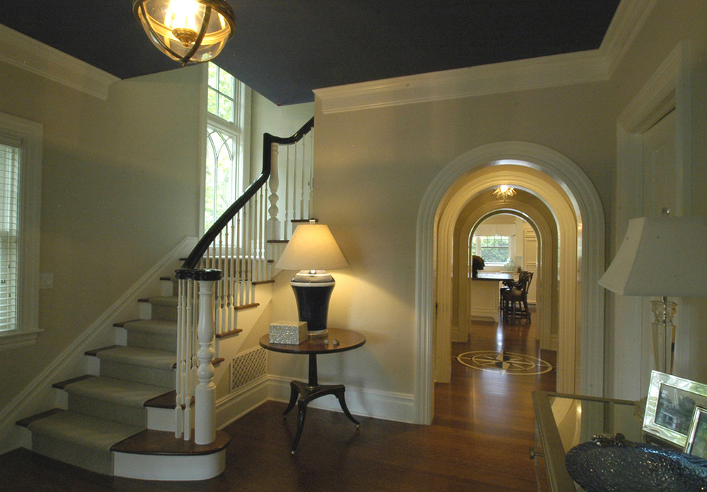 Cette photo montre un grand hall d'entrée chic avec un mur beige, un sol en bois brun, une porte simple, une porte noire et un sol marron.