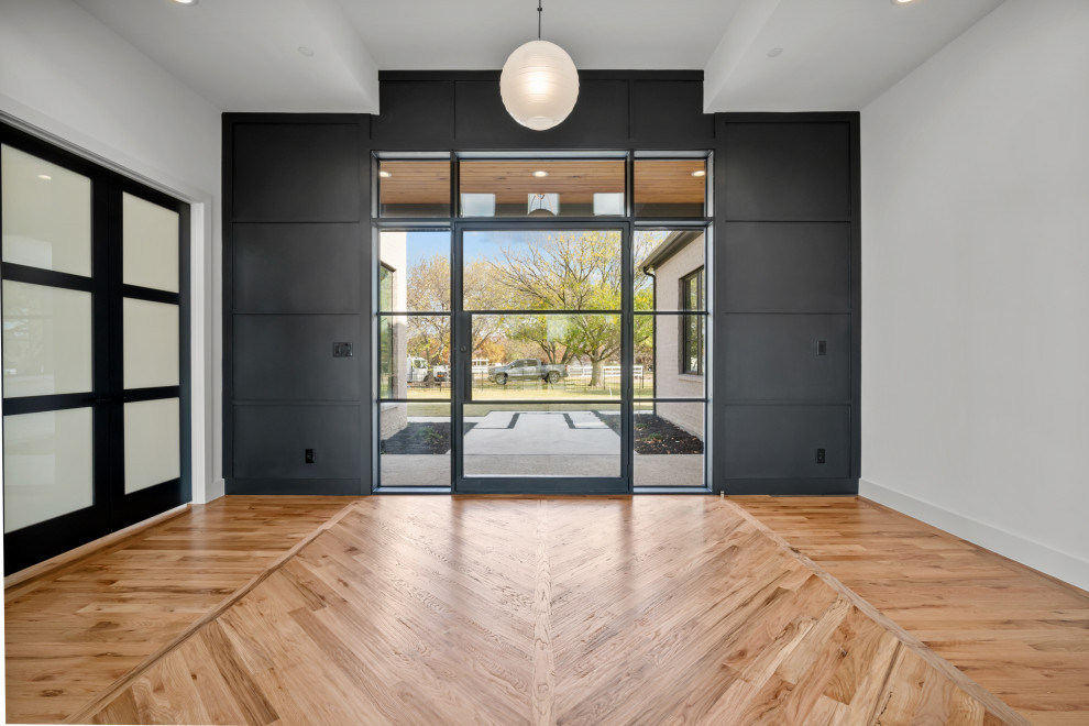 Idee per un ingresso minimalista di medie dimensioni con pareti nere, parquet chiaro, una porta a pivot, una porta nera, pavimento beige e boiserie