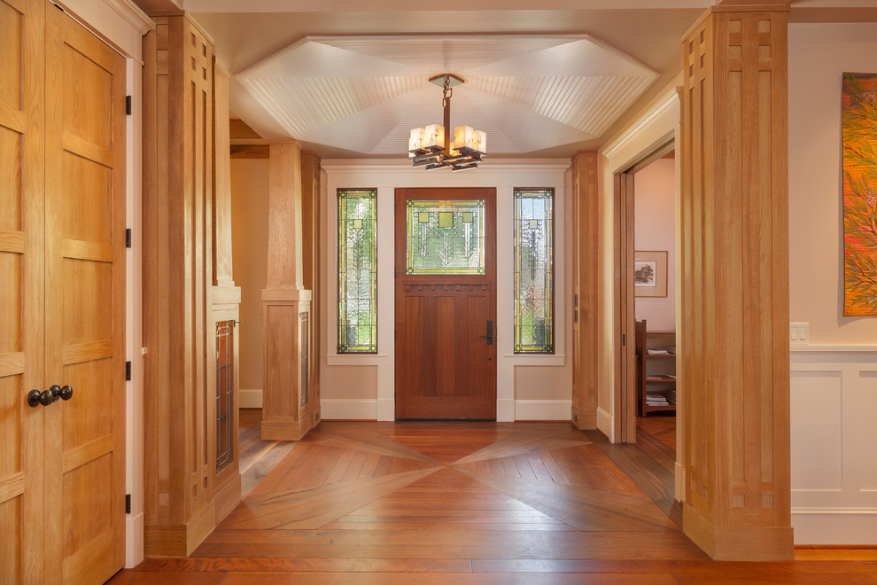 Modelo de distribuidor de estilo americano grande con paredes beige, suelo de madera en tonos medios, puerta simple y puerta de madera en tonos medios