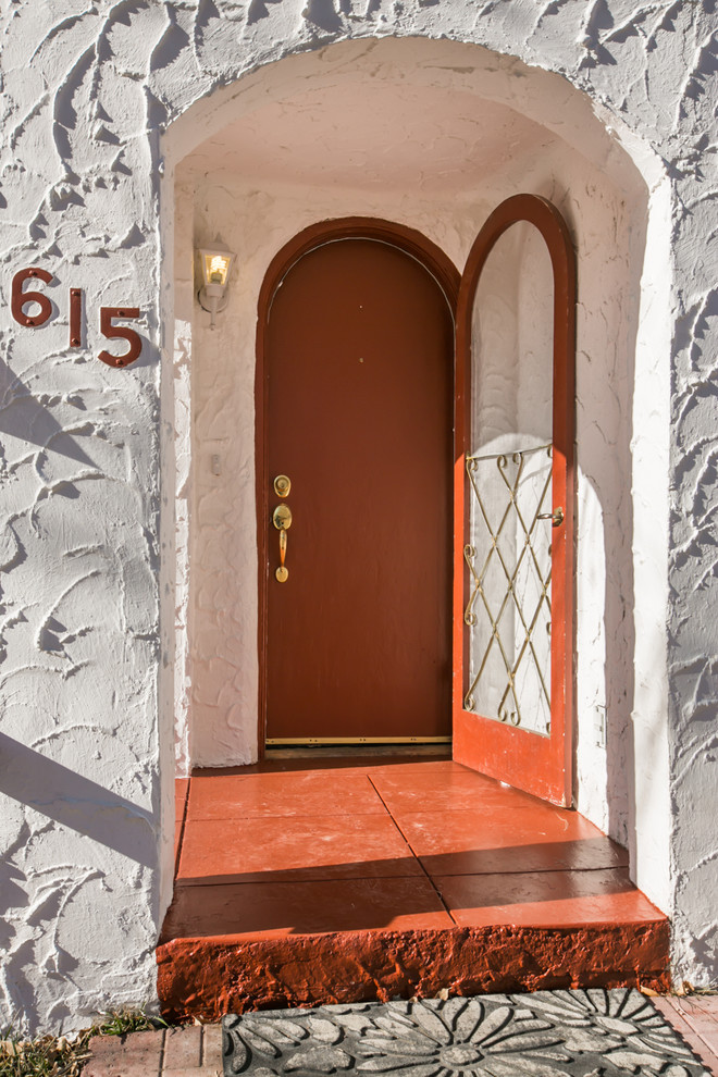 Cette photo montre une petite porte d'entrée méditerranéenne avec un mur blanc, sol en béton ciré, une porte simple et une porte rouge.