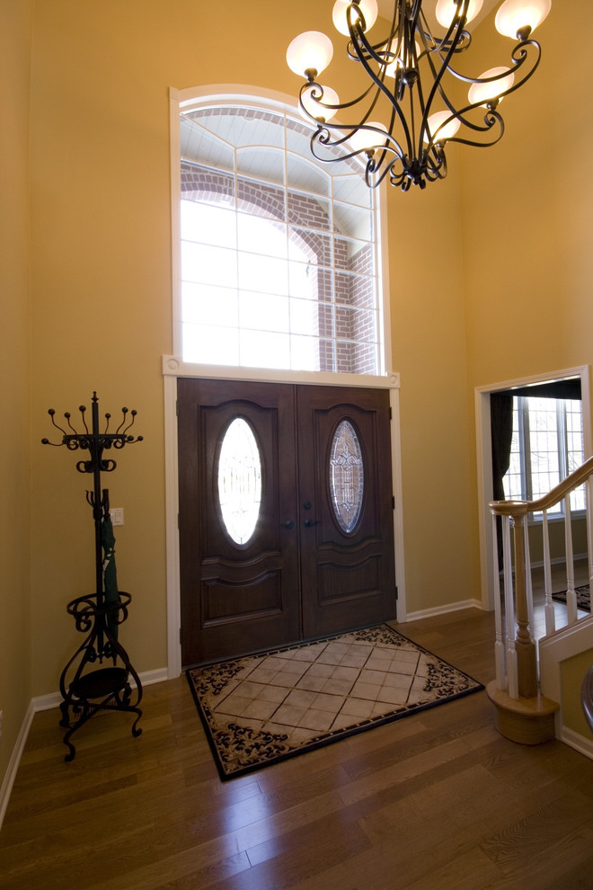 Immagine di un grande ingresso minimal con pareti gialle, pavimento in legno massello medio, una porta a due ante e una porta in legno scuro