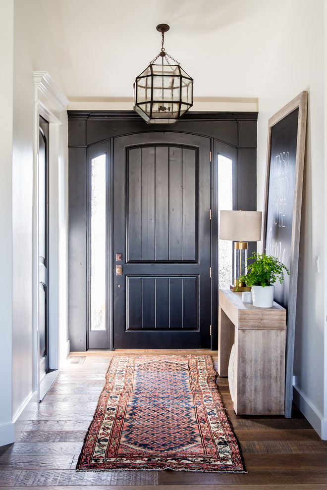 На фото: маленькая входная дверь в стиле неоклассика (современная классика) с белыми стенами, паркетным полом среднего тона, одностворчатой входной дверью и черной входной дверью для на участке и в саду
