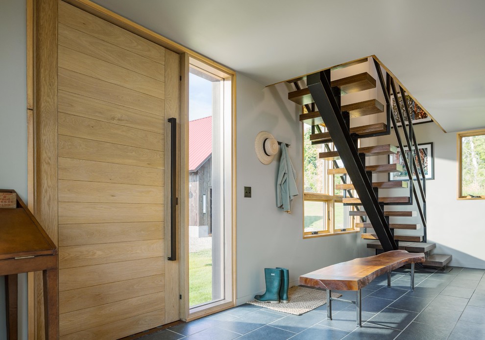 Cette image montre un hall d'entrée minimaliste de taille moyenne avec un mur gris, un sol en carrelage de porcelaine, une porte pivot, une porte en bois clair et un sol gris.