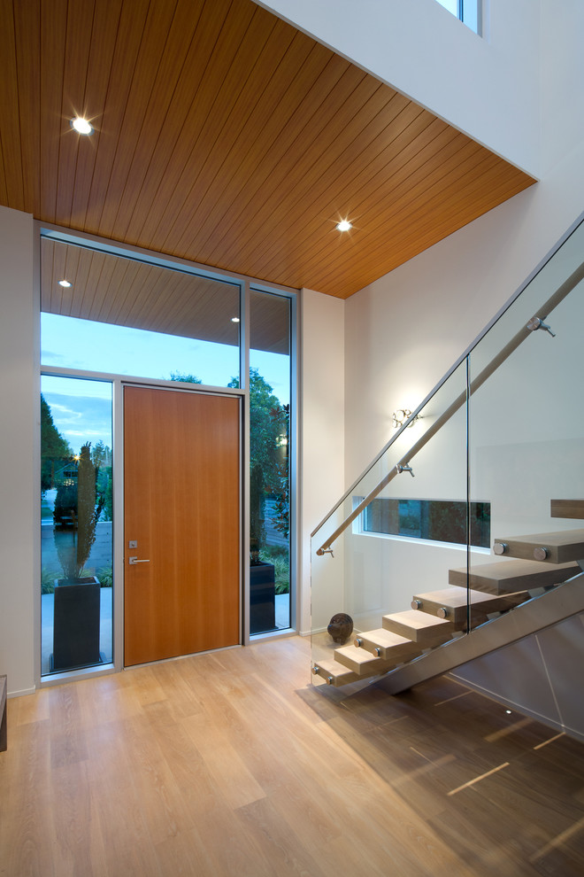 Idée de décoration pour un hall d'entrée minimaliste avec un mur blanc, parquet clair et une porte en bois brun.