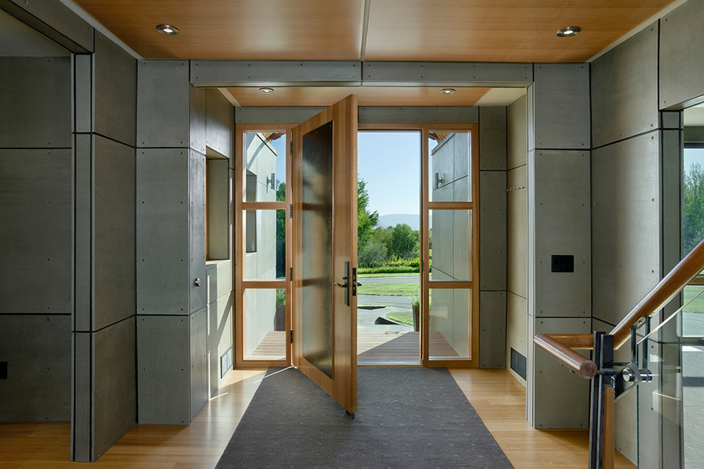 Foto på en funkis ingång och ytterdörr, med grå väggar, ljust trägolv, en enkeldörr och metalldörr