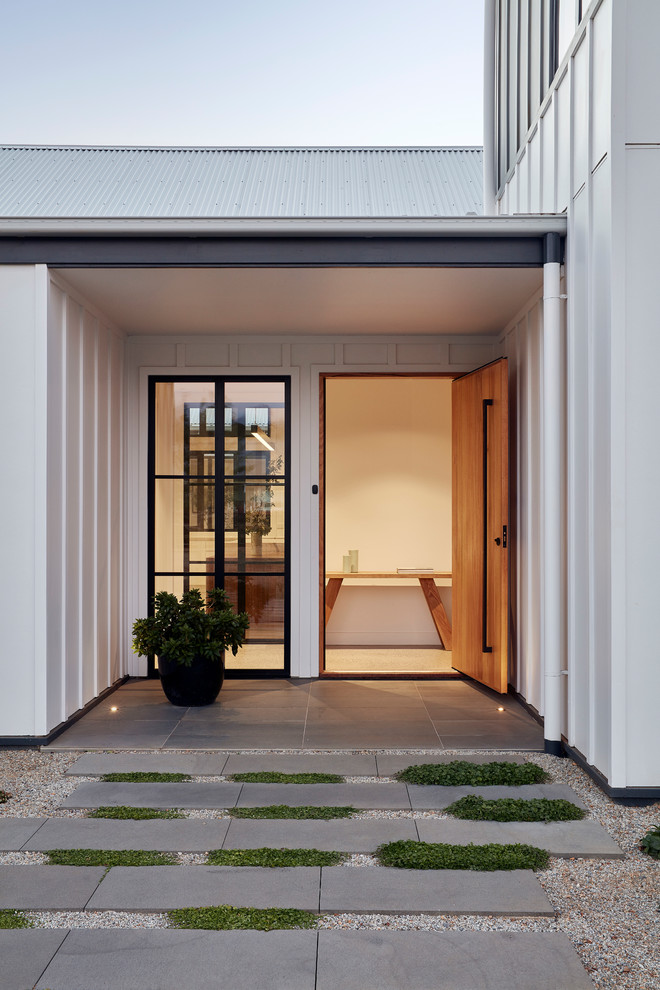 Cette image montre une porte d'entrée rustique de taille moyenne avec un mur blanc, sol en béton ciré, une porte pivot, une porte en bois clair et un sol blanc.