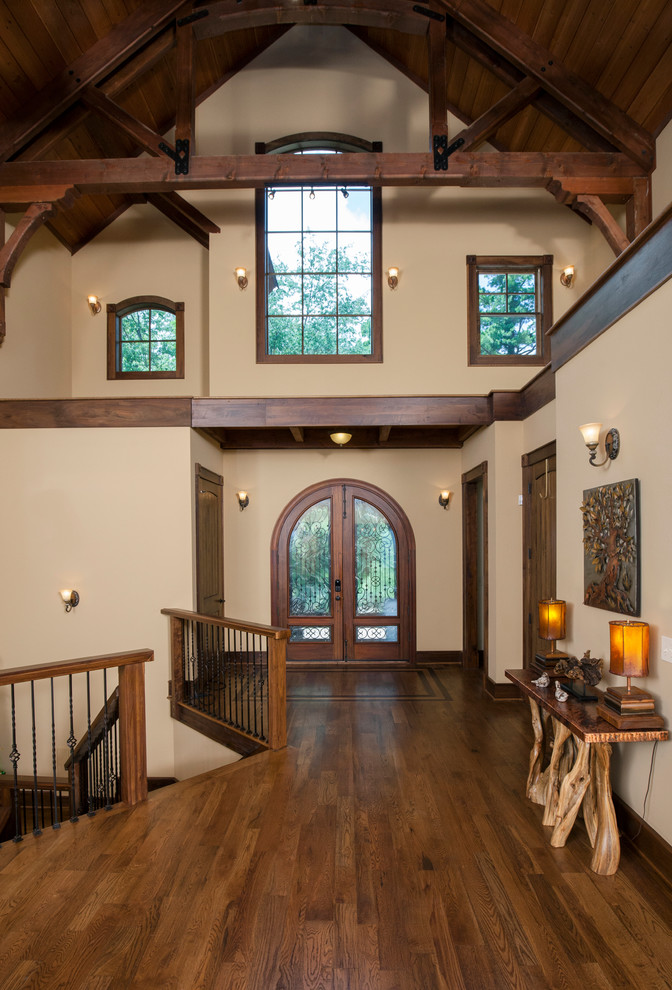 Aménagement d'un grand hall d'entrée montagne avec un mur beige, un sol en bois brun, une porte double et une porte en bois brun.