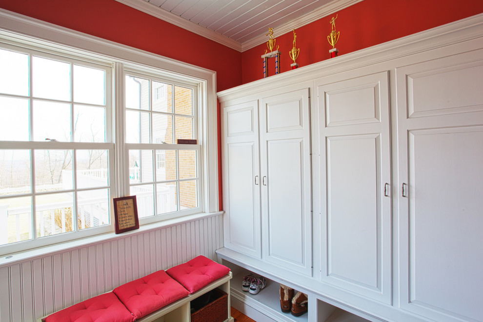 Aménagement d'une petite entrée classique avec un mur rouge, parquet foncé, une porte simple et une porte blanche.