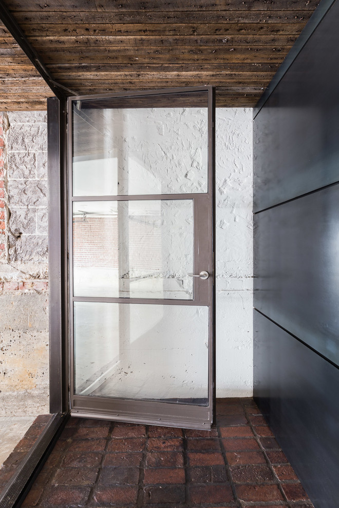 Idee per una porta d'ingresso industriale di medie dimensioni con pareti bianche, una porta in vetro, una porta singola, pavimento marrone e pavimento in mattoni
