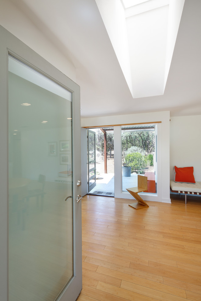 Imagen de entrada minimalista con paredes blancas, suelo de madera clara y puerta de vidrio