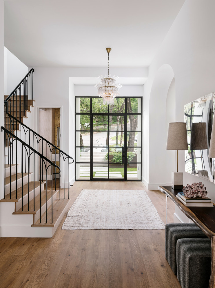This is an example of a large mediterranean foyer in Austin with white walls, light hardwood flooring, a single front door, a black front door and beige floors.