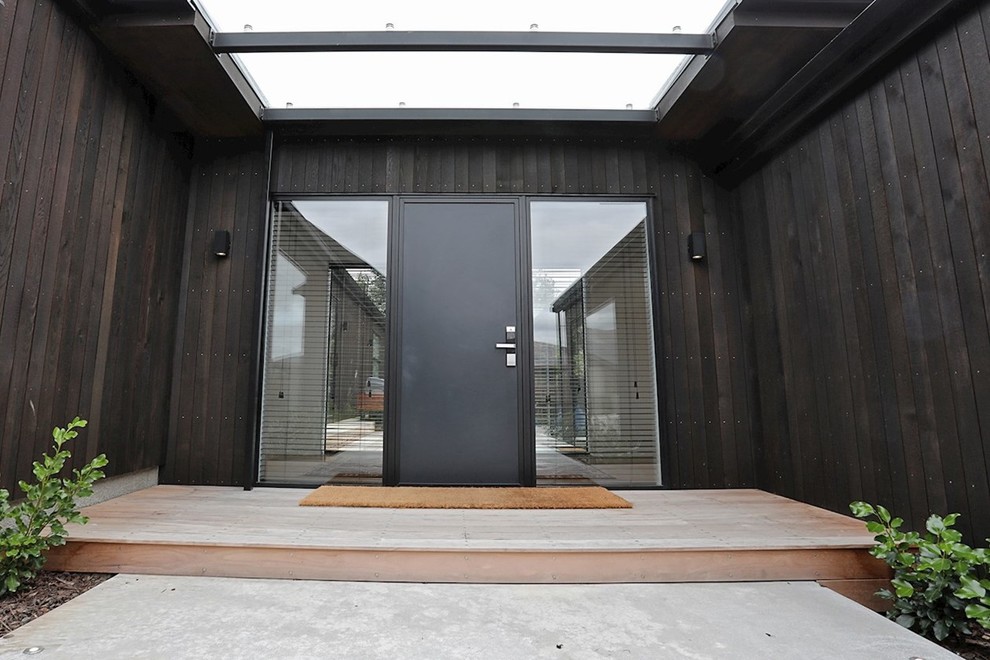 Cette image montre une grande porte d'entrée minimaliste avec un mur marron, parquet foncé, une porte simple, une porte noire et un sol marron.