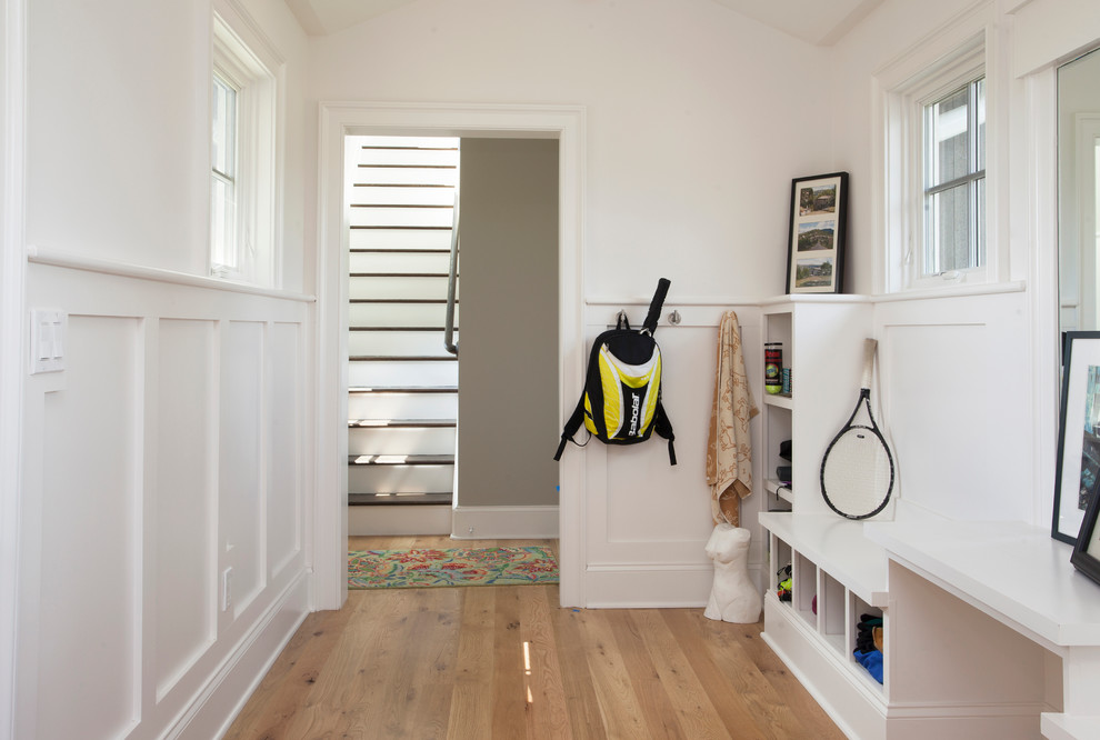 Inspiration pour une entrée minimaliste avec un vestiaire, un mur blanc et un sol en bois brun.