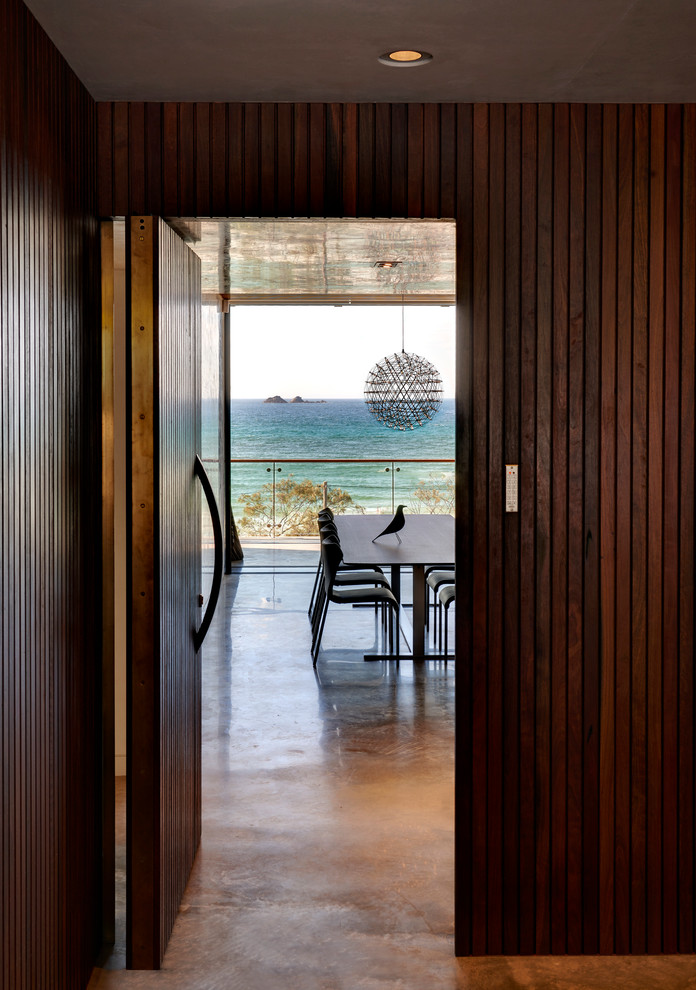 Cette photo montre une porte d'entrée bord de mer de taille moyenne avec un mur blanc, sol en béton ciré, une porte pivot et une porte en bois brun.