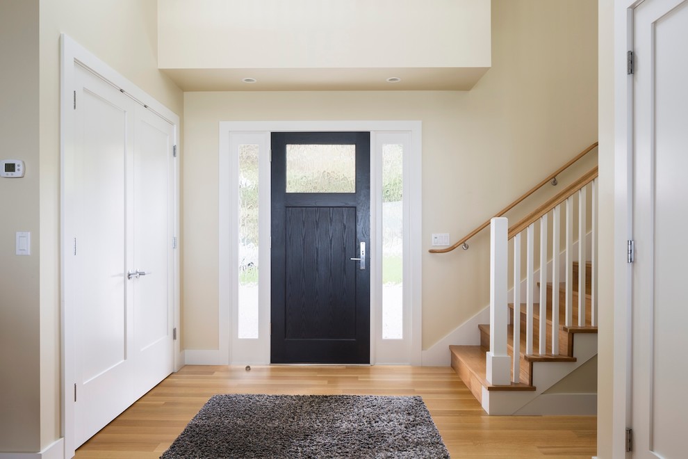 Esempio di un ingresso design di medie dimensioni con pareti beige, pavimento in legno massello medio, una porta singola e una porta nera