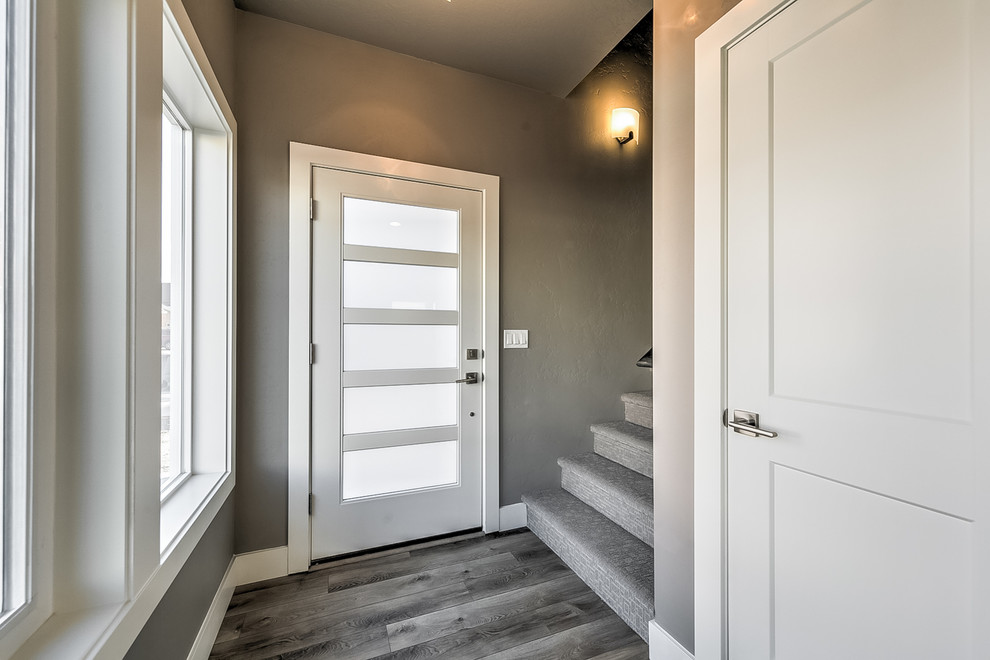 Modern inredning av en liten foajé, med grå väggar, laminatgolv, en enkeldörr, en orange dörr och grått golv