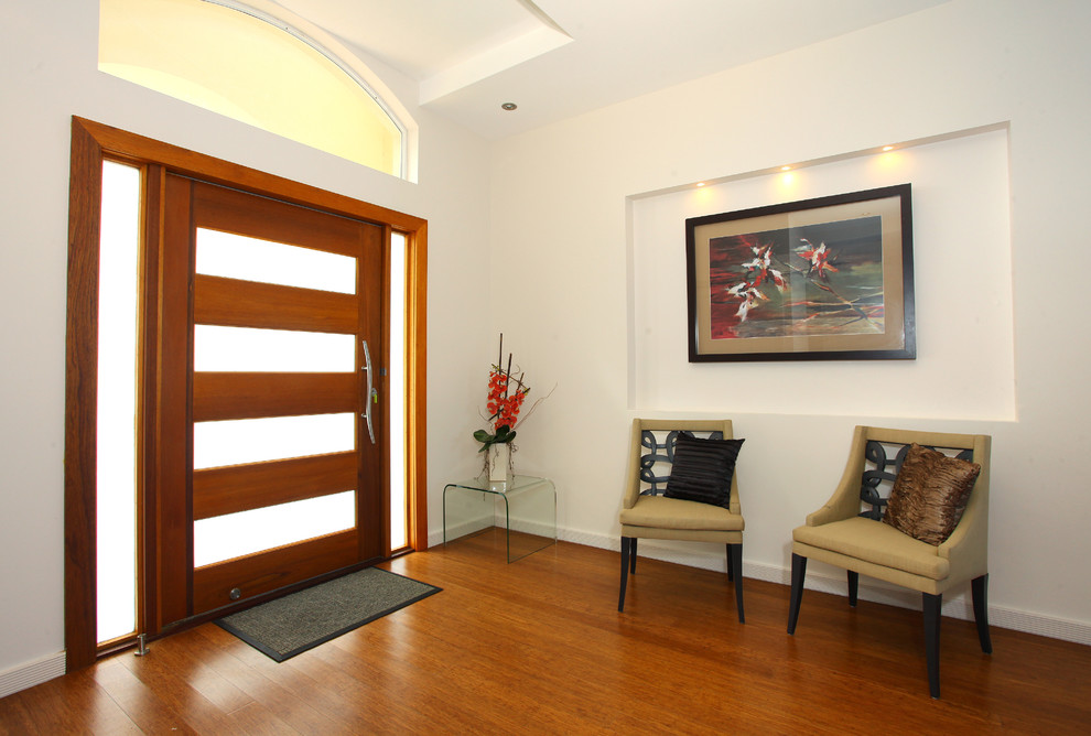 Imagen de distribuidor contemporáneo grande con paredes blancas, suelo de bambú, puerta pivotante y puerta de madera en tonos medios