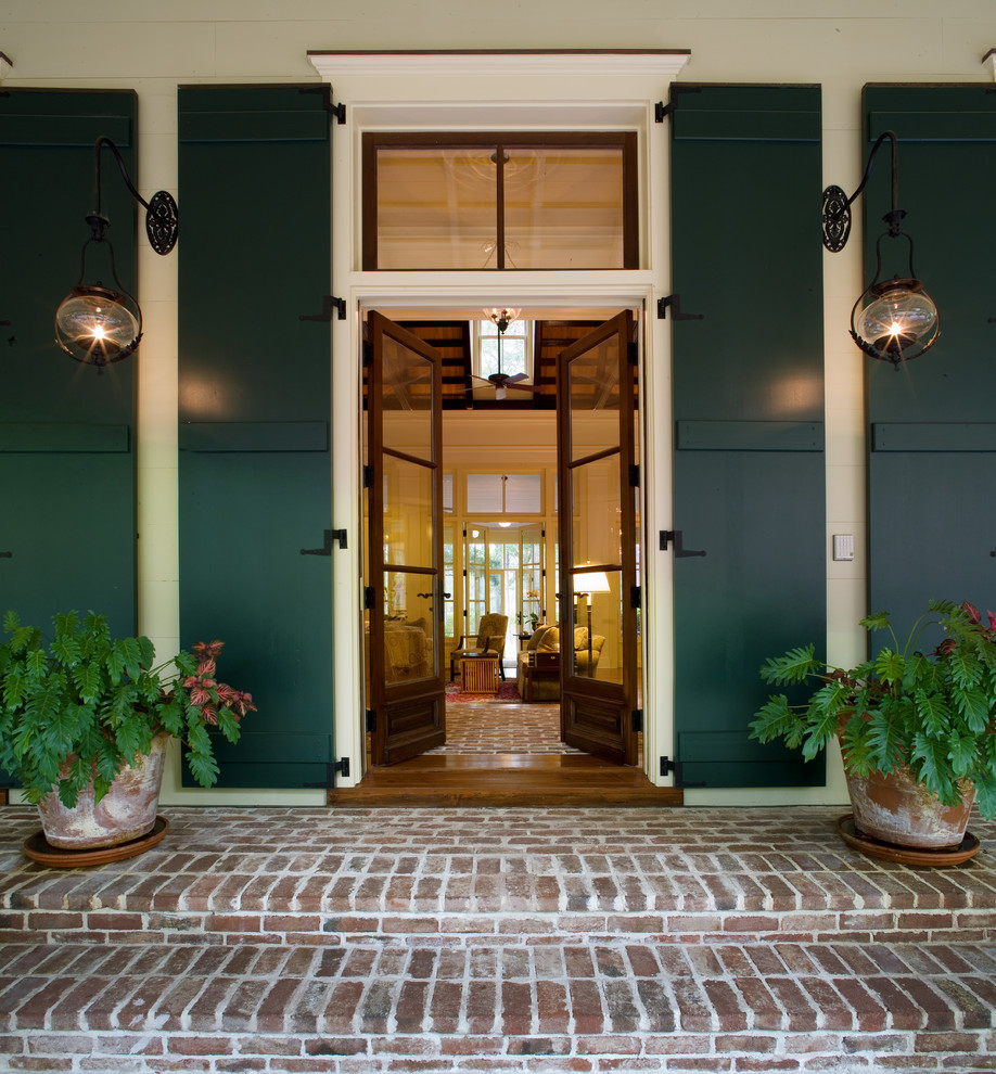 На фото: входная дверь: освещение в классическом стиле с двустворчатой входной дверью, стеклянной входной дверью и кирпичным полом с