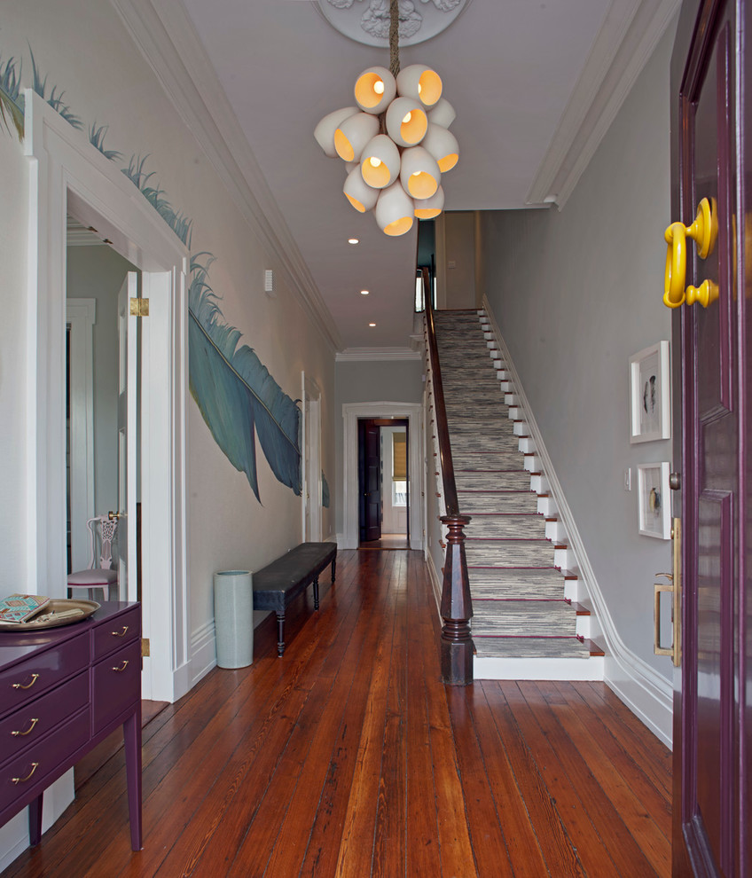 Cette image montre un hall d'entrée bohème de taille moyenne avec un mur gris, un sol en bois brun, une porte simple, une porte violette et un sol marron.