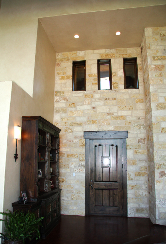 Cette image montre un hall d'entrée chalet de taille moyenne avec un mur beige, sol en béton ciré et une porte en bois foncé.