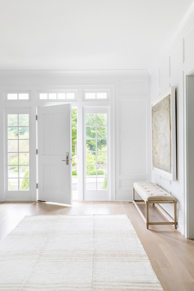 Großes Klassisches Foyer mit weißer Wandfarbe, hellem Holzboden, Einzeltür, weißer Haustür und braunem Boden in New York