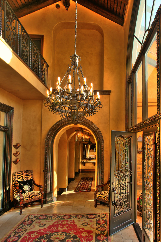 Aménagement d'un grand hall d'entrée méditerranéen avec un mur marron, un sol en travertin, une porte double et une porte métallisée.