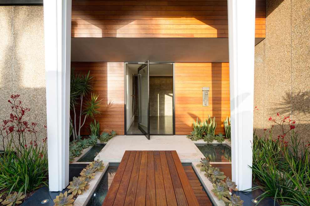 Réalisation d'une porte d'entrée design avec un mur marron, une porte pivot, une porte en verre et un sol beige.