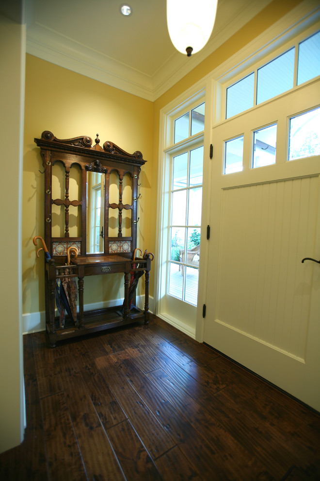 Diseño de puerta principal tradicional de tamaño medio con paredes amarillas, suelo de madera oscura, puerta simple y puerta blanca