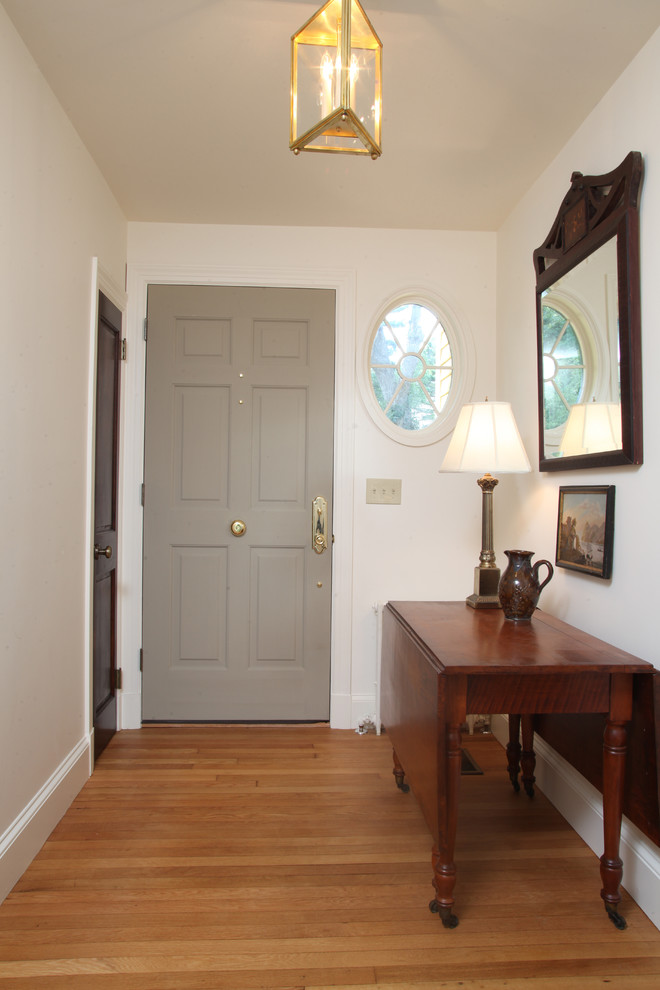 Cette photo montre une petite porte d'entrée chic avec un mur jaune, un sol en bois brun, une porte simple et une porte grise.